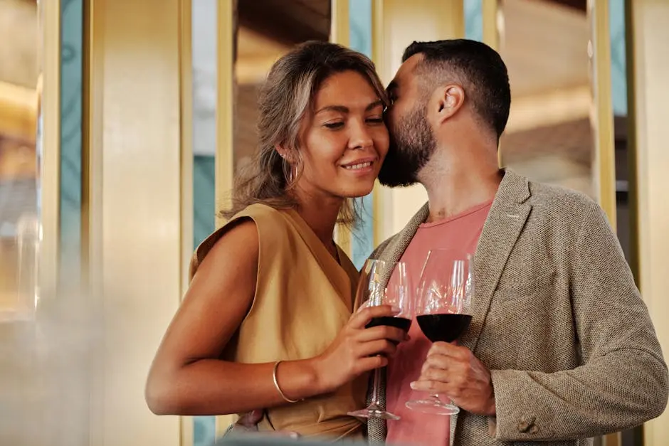 A couple embraces while holding wine glasses in an intimate indoor setting.