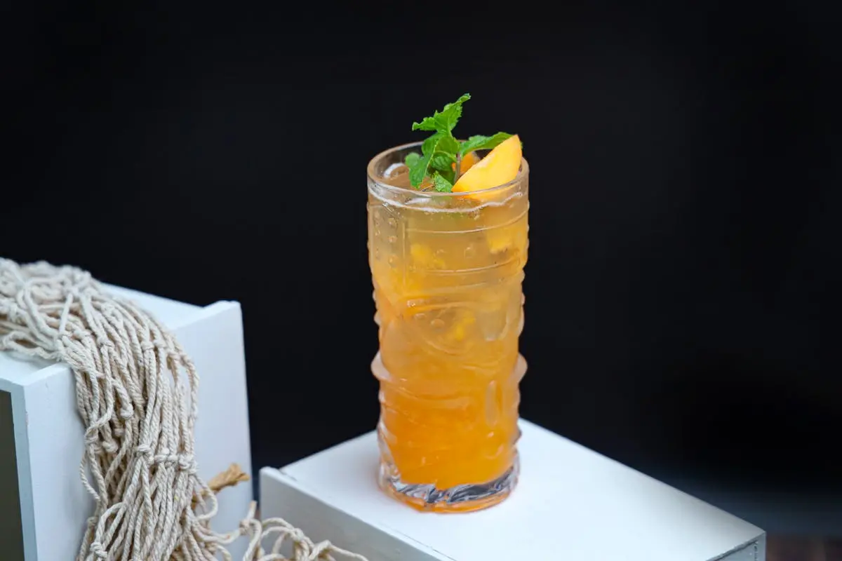 A tall glass of iced lemon and mint drink presented on a white surface with a dark background.