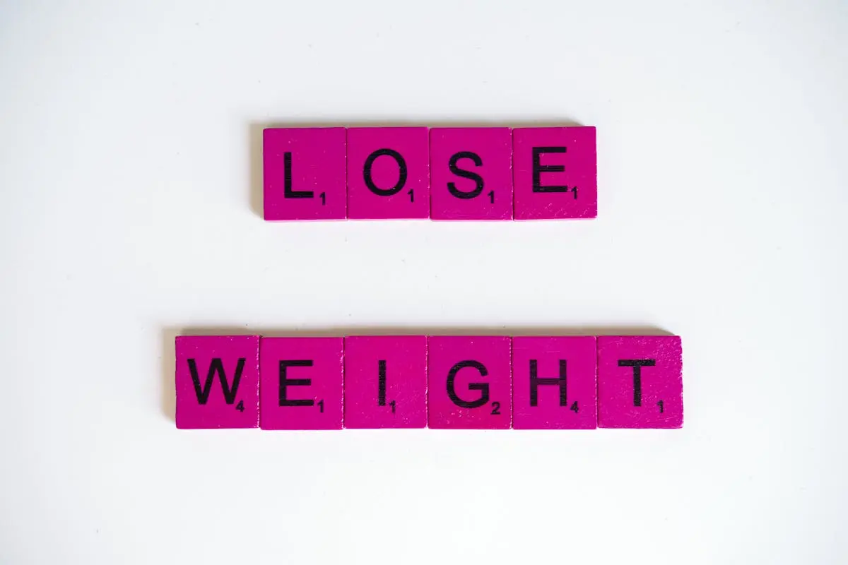 Creative image of the phrase ‘Lose Weight’ spelled with Scrabble tiles on a white background.