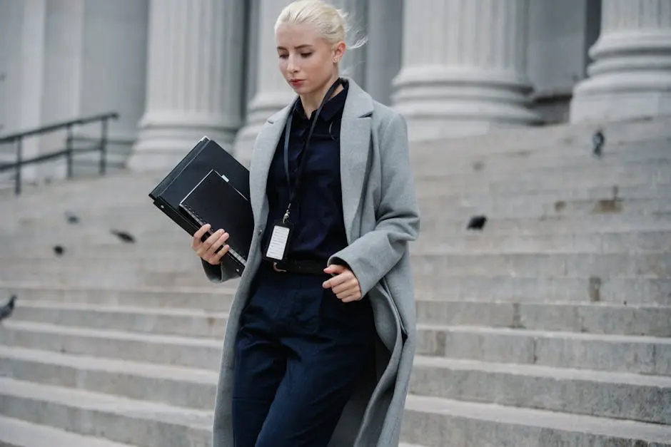 Professional woman in formal attire walking down courthouse steps holding folders outdoors.