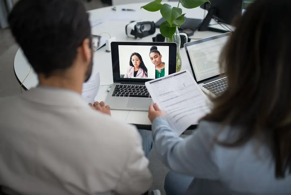 Two professionals conduct a virtual job interview using laptops in a modern office.