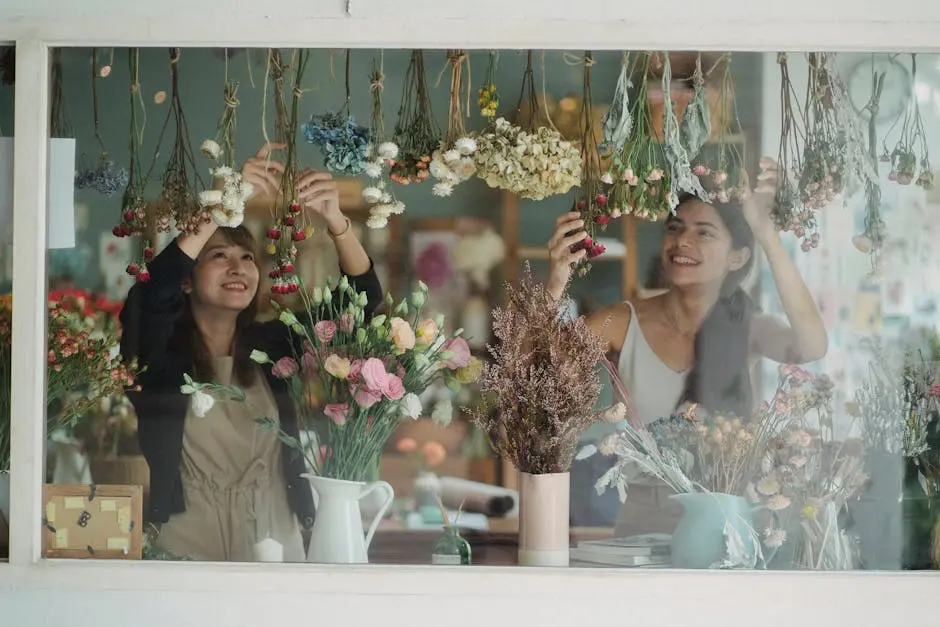 Two happy florists decorating a shop with vibrant dried flowers, creating a lovely floral arrangement.