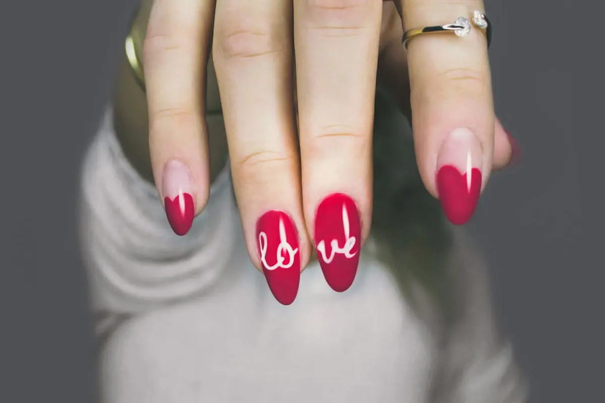 Vibrant red nails with ‘love’ art on a woman’s hand, showcasing elegant style and design.