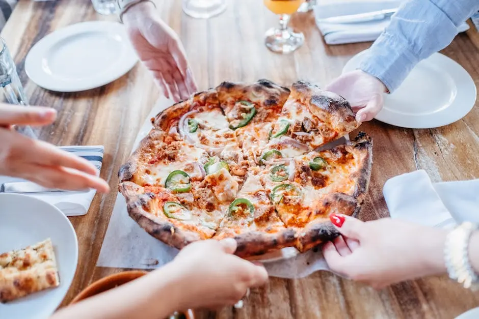 Friends sharing a hot pizza with sliced jalapeños and toppings at a wooden table.