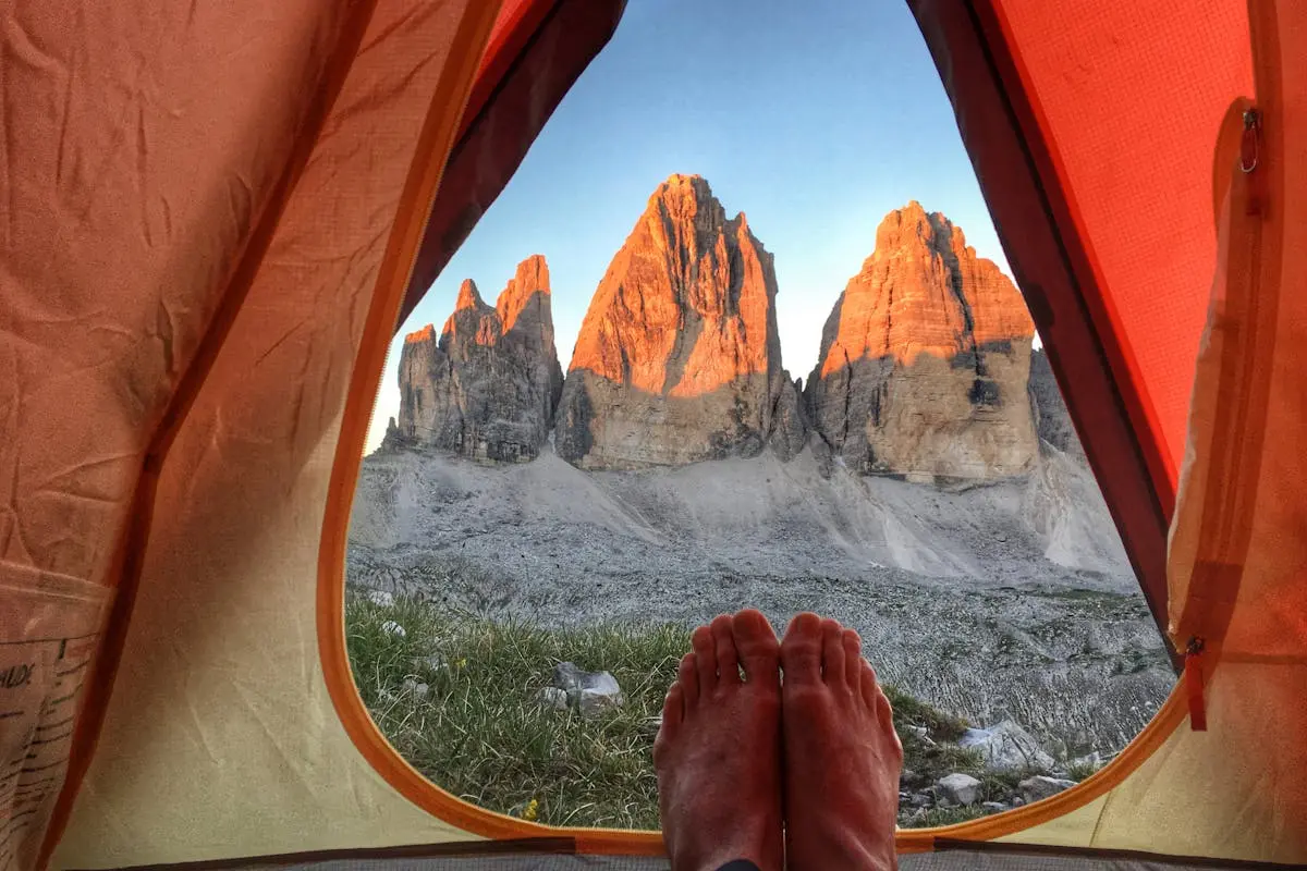 View of Tre Cime di Lavaredo glowing at sunrise from a camping tent in the Italian Alps.