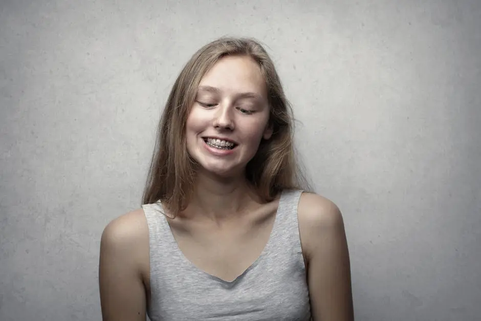 Portrait of a cheerful young woman with braces, smiling with closed eyes against a neutral background.