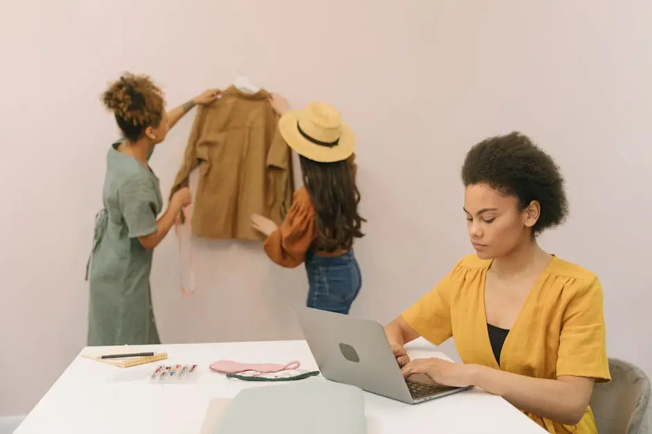 Three women working together indoors in a creative business environment, discussing fashion and using technology.