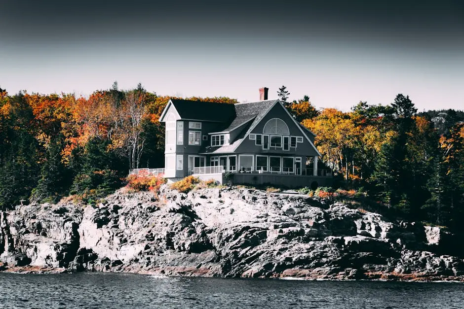A scenic coastal home on a rocky cliff surrounded by vibrant autumn trees.