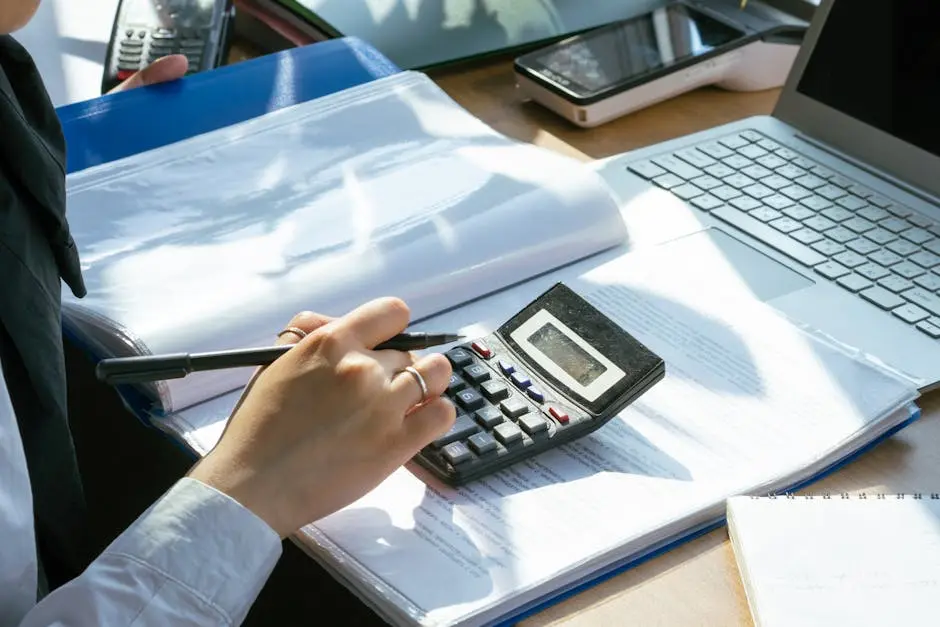 A person working on financial calculations using a calculator and laptop at an office desk. medical equipment