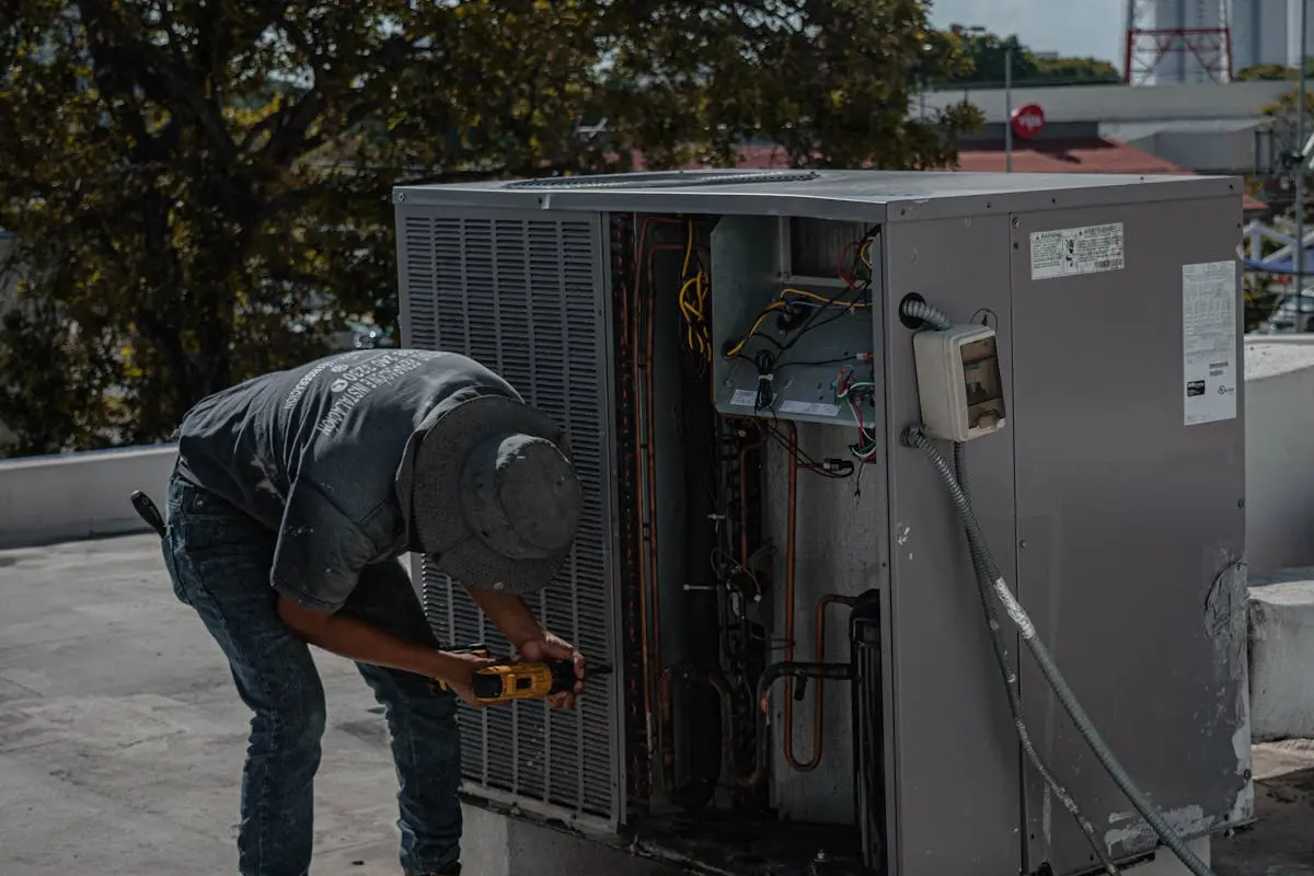 A technician is repairing an air conditioning unit on a rooftop, demonstrating skilled manual work.