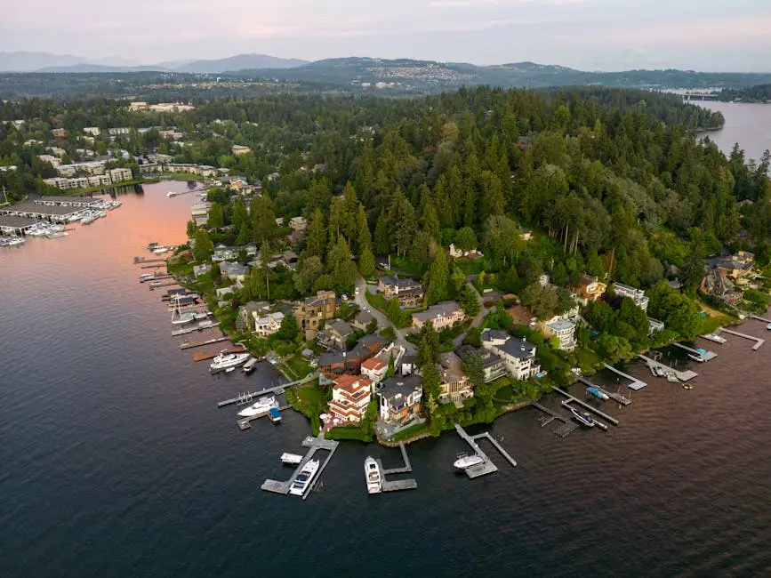 Scenic aerial view of waterfront homes, marina, lush greenery, and distant mountains during sunset.