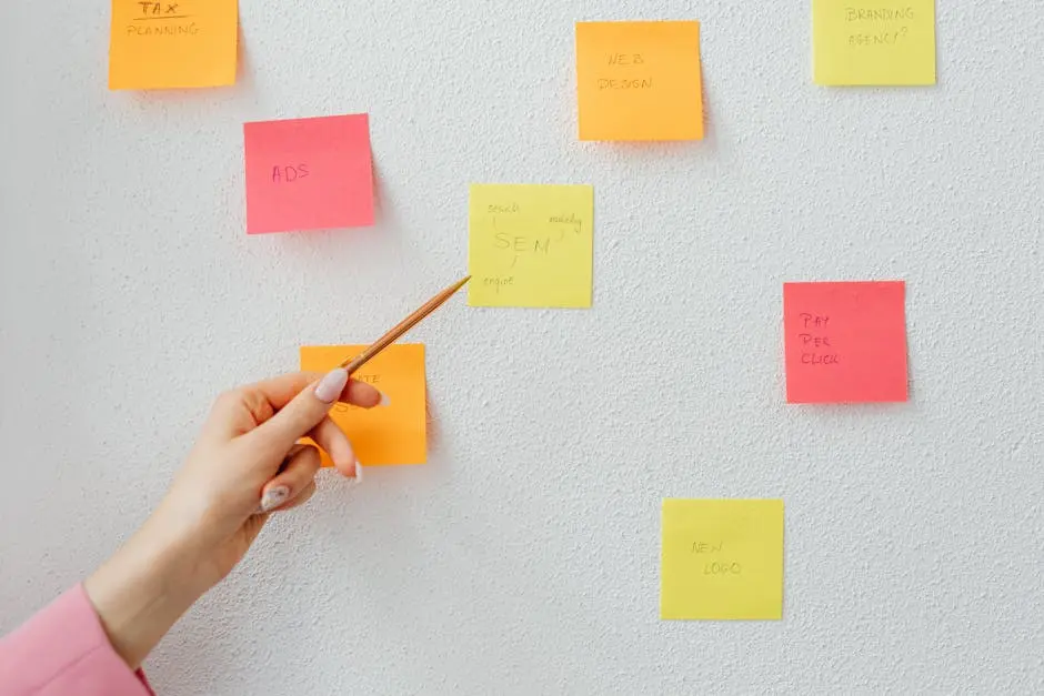 Hand pointing at colorful sticky notes with business concepts on a wall.