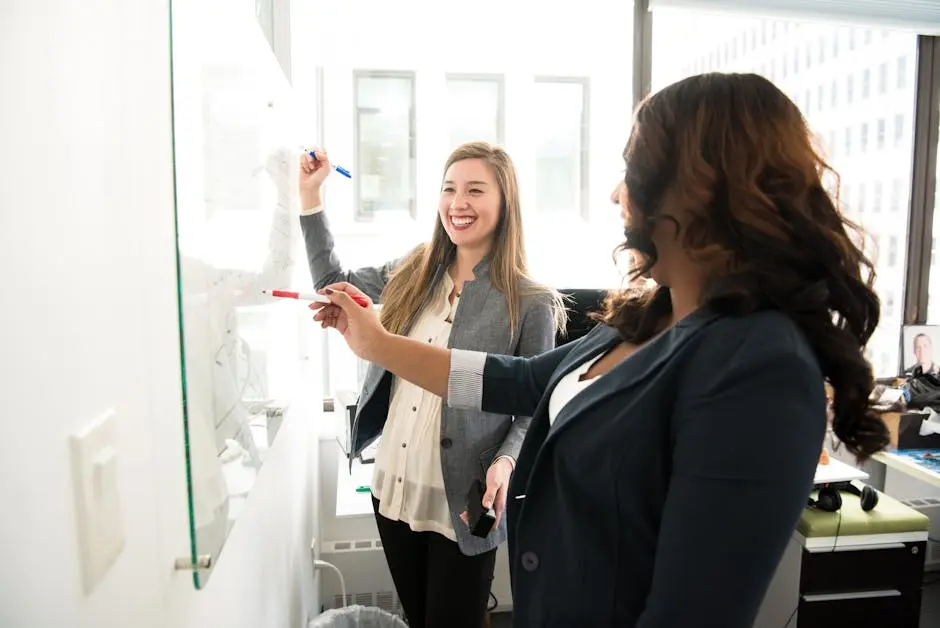Two professional women discussing ideas on a whiteboard in a modern office setting. business coach