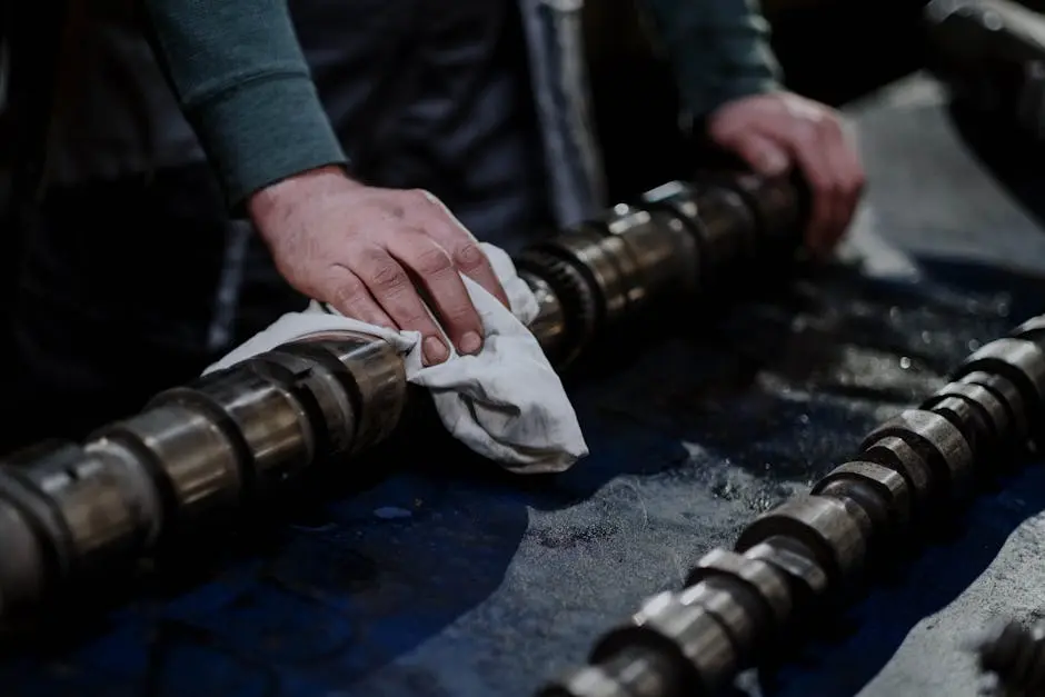 Close-up of a mechanic cleaning a camshaft with a cloth in an industrial setting.