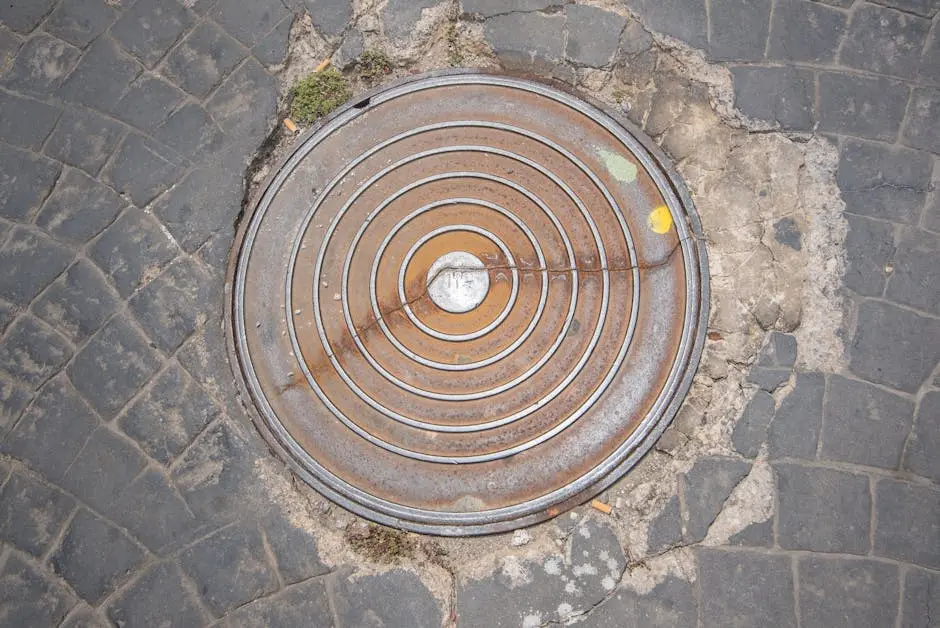 A rusty manhole cover surrounded by cobblestones with visible peeling paint.