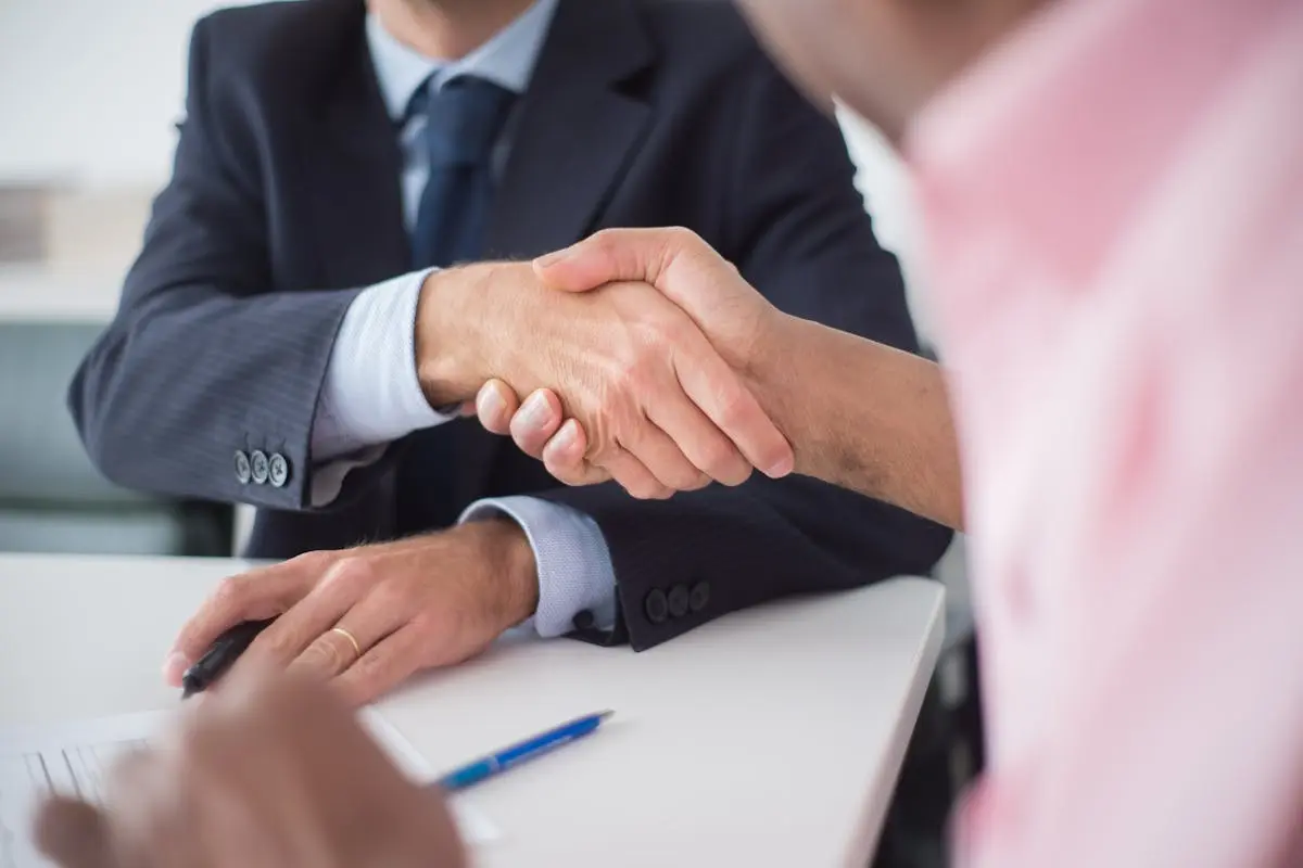 Two businessmen shaking hands across table, symbolizing agreement and partnership in an office environment. How to Buy a Small Business with No Money