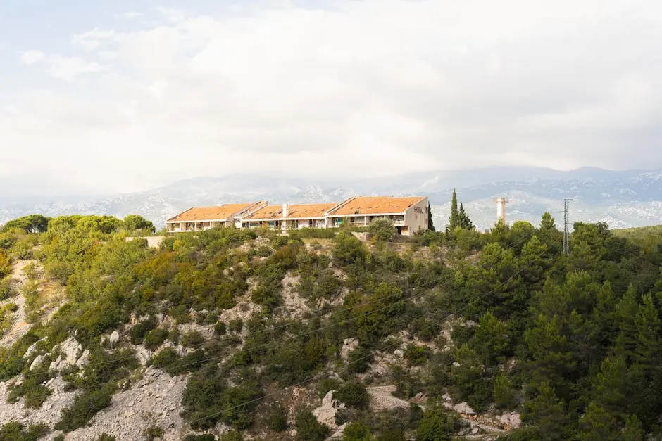 Rustic houses on a mountain slope surrounded by lush greenery and distant mountains in summer.