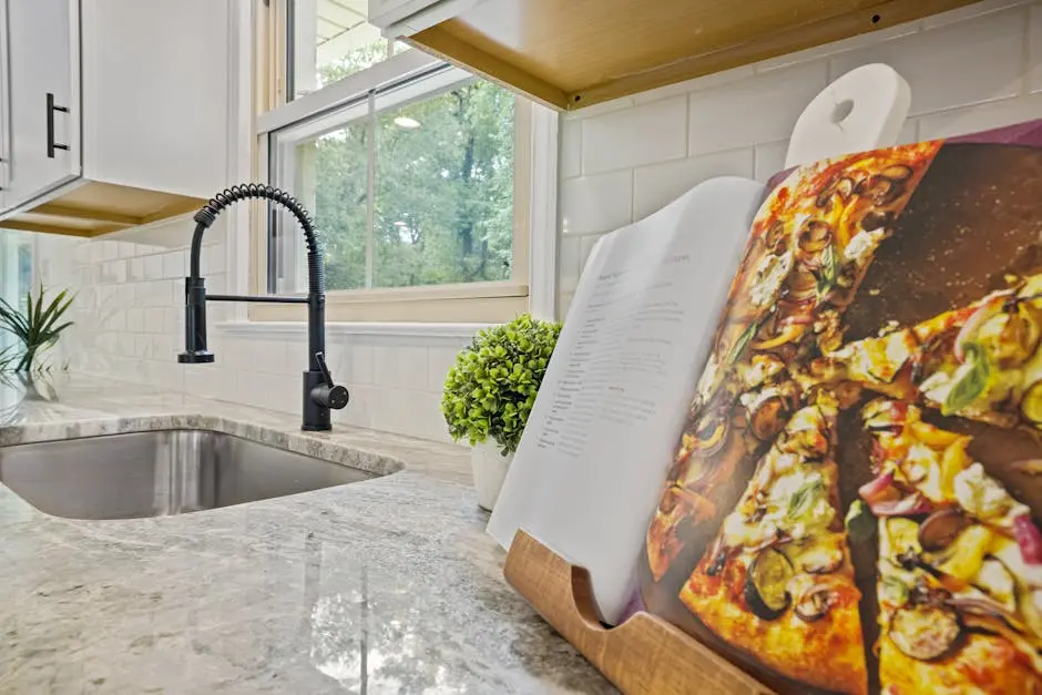 Stylish kitchen featuring a marble countertop, modern sink, and an open cookbook with a pizza recipe.