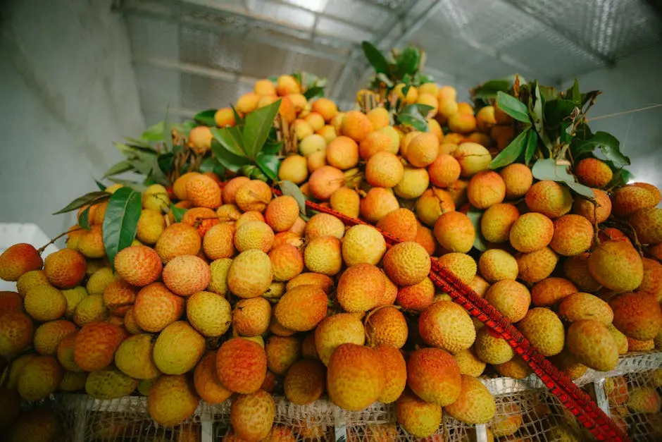 A vibrant pile of freshly harvested lychees with green leaves, showcasing their textured skin and natural color.