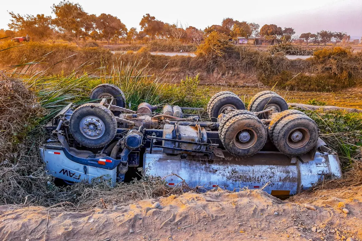 A truck overturned by the roadside on a rural dirt path during daytime.