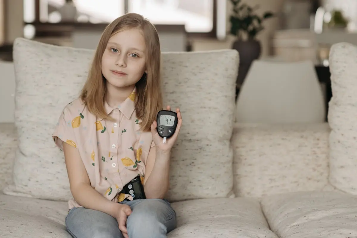 A girl sitting on a couch displaying a glucometer, highlighting health awareness.