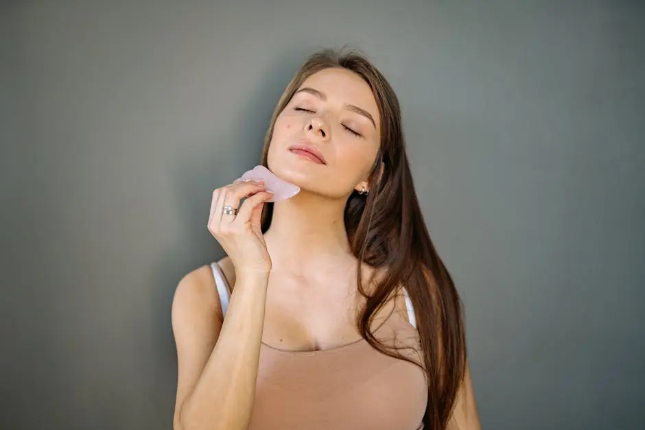 Woman using a gua sha tool on her face, eyes closed, reflecting a serene skincare routine.