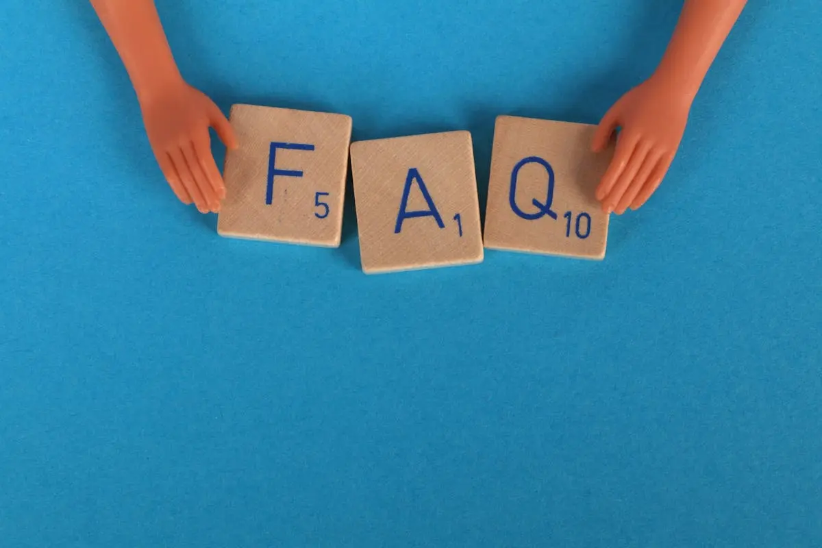 Flat lay of scrabble tiles spelling ‘FAQ’ with toy hands on a blue background, creating a conceptual image.
