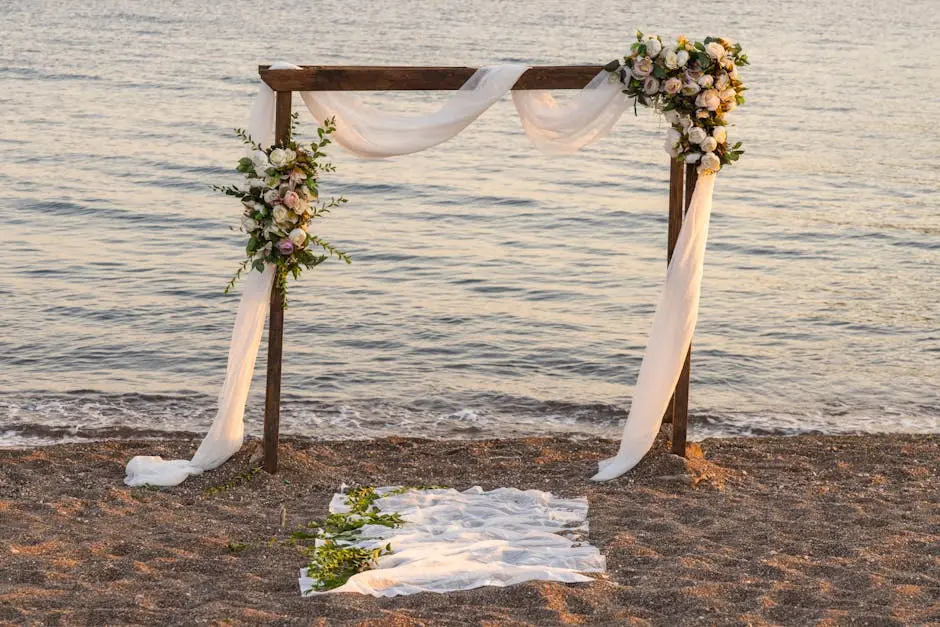 Romantic beach wedding setup with floral arch and ocean backdrop.