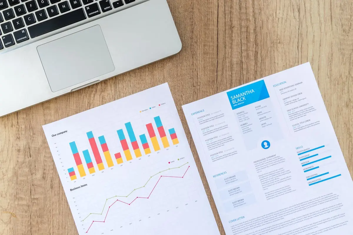 Top view of a laptop, charts, and resume on a wooden desk, showcasing business analysis and job application. How to Buy a Small Business with No Money