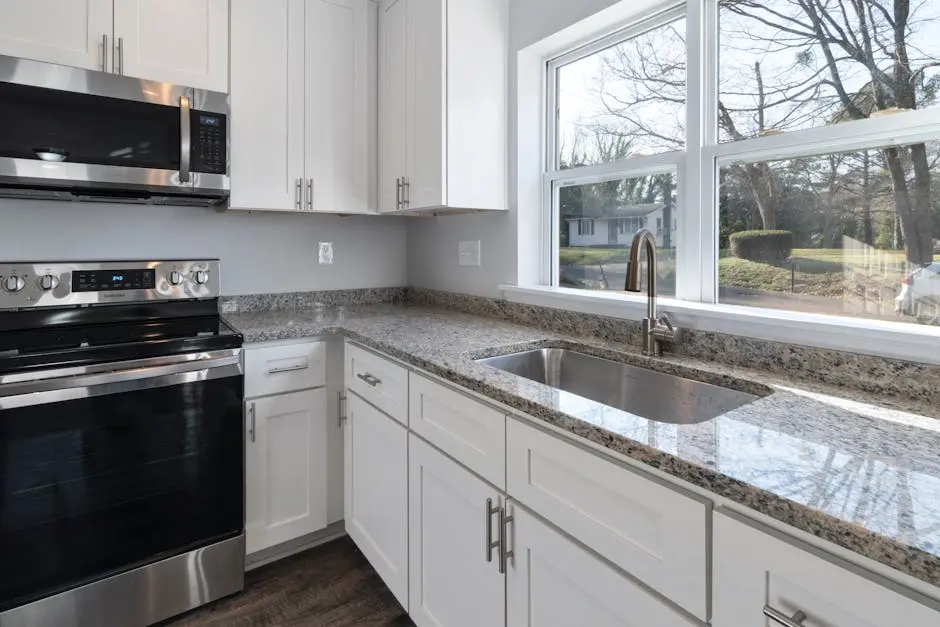 Bright kitchen showcasing granite countertops, stainless steel appliances, and large windows.