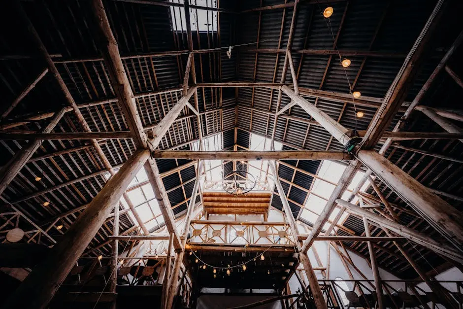 A dramatic view inside a rustic barn showcasing wooden beams and steel framework.