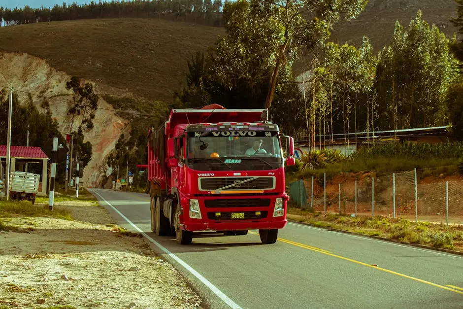 Red truck traveling on a scenic road with mountains and greenery, offering a sense of adventure.