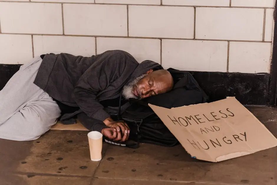 A homeless man sleeping on the street with a cardboard sign, capturing urban hardship.