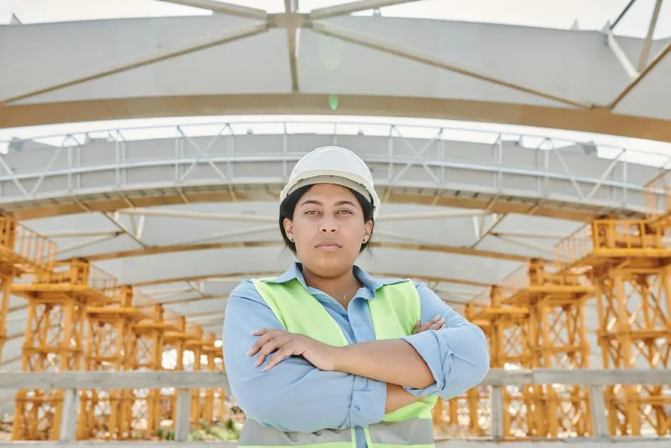 Female engineer in safety gear at a construction site with steel structure background.