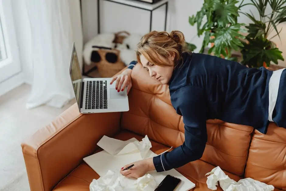 Woman resting on a couch with laptop, surrounded by papers, depicting stressed remote work lifestyle.