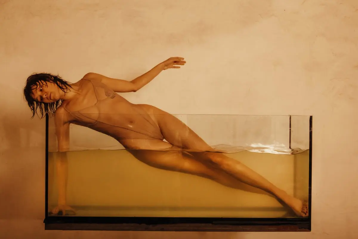 An evocative photograph of a woman posing in a water tank in a studio setting.