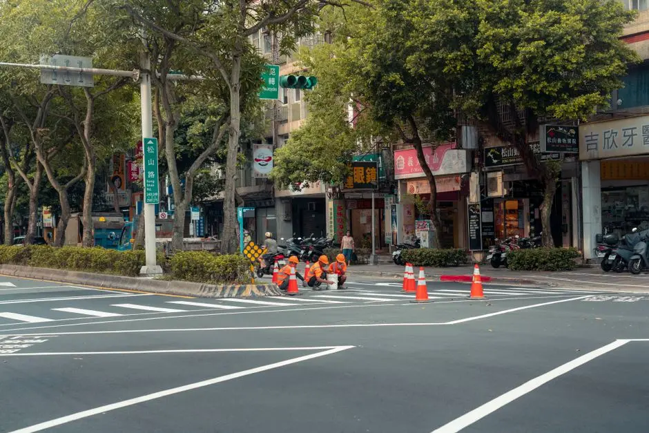 Workers painting road lanes in a bustling city intersection.