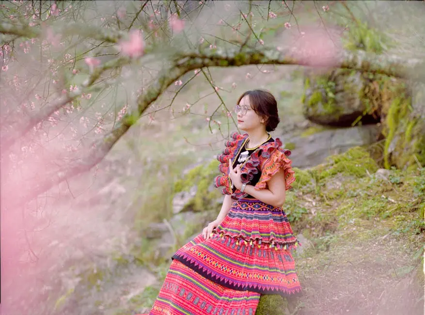 Woman in colorful traditional dress in a serene spring blossom setting.