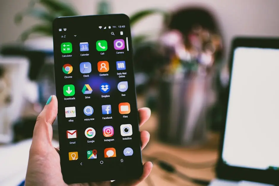 A close-up image of a person&rsquo;s hand holding a smartphone displaying various popular apps.