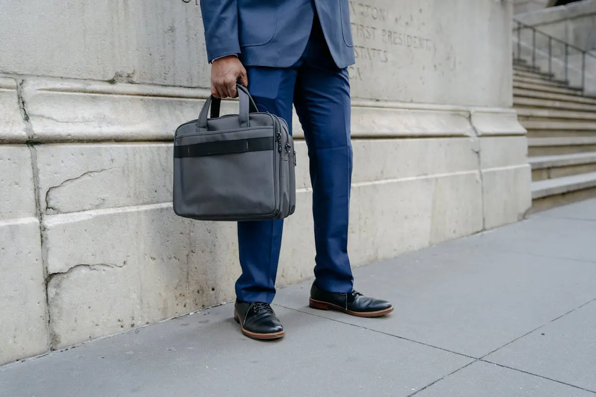 Businessman in blue suit holding a briefcase outside a stately building, urban setting.