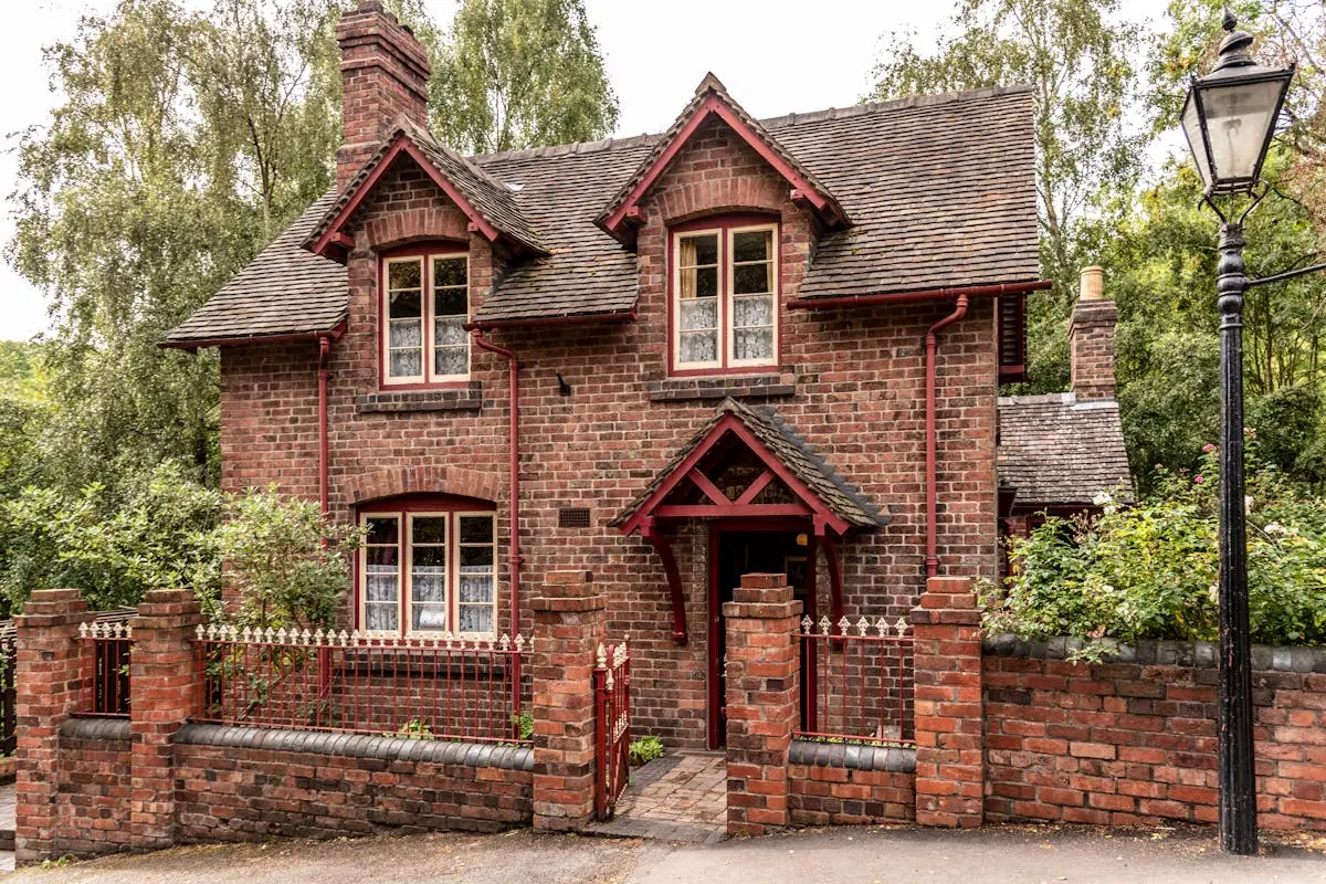A picturesque brick cottage in England, surrounded by lush greenery and a charming fence.