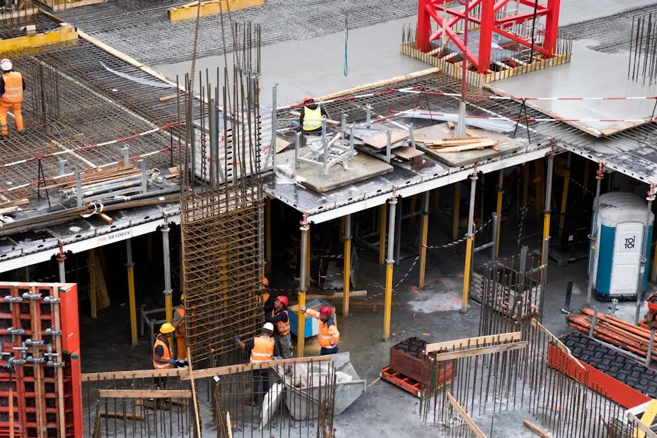 Workers in high visibility gear at a busy construction site with scaffolding and steel frames.