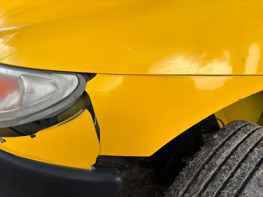 Close-up image of a yellow car’s damaged front bumper and headlight for insurance or accident concept.