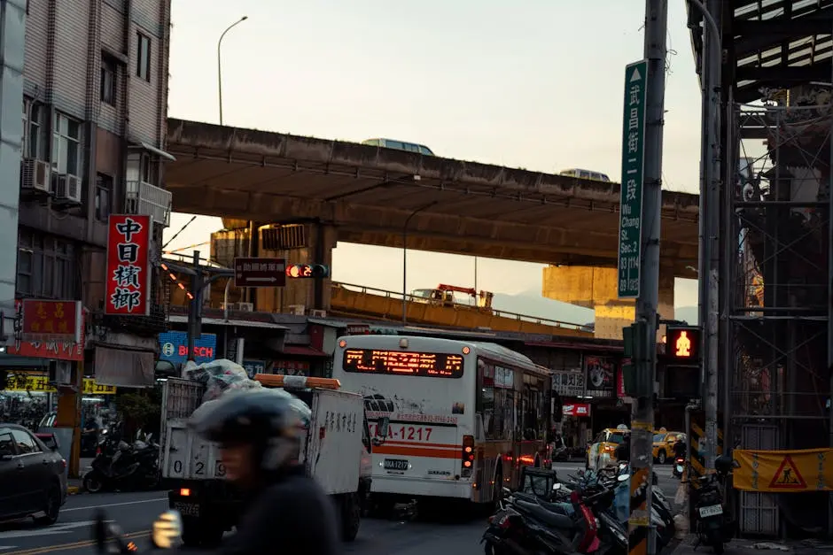 A lively city street scene featuring traffic, including a bus, with an elevated road in the background.