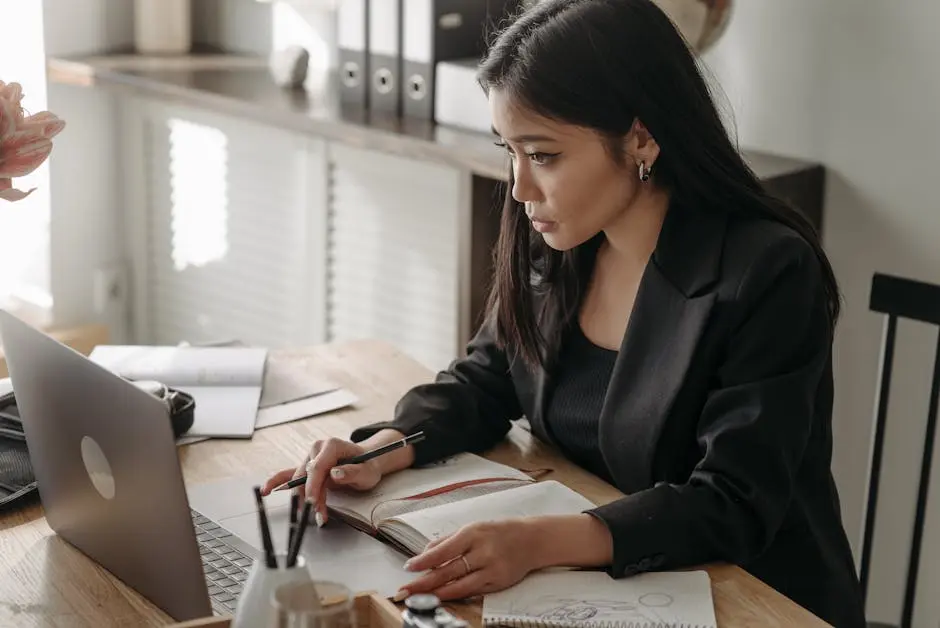 Young woman in blazer taking notes during an online lecture at home workspace.