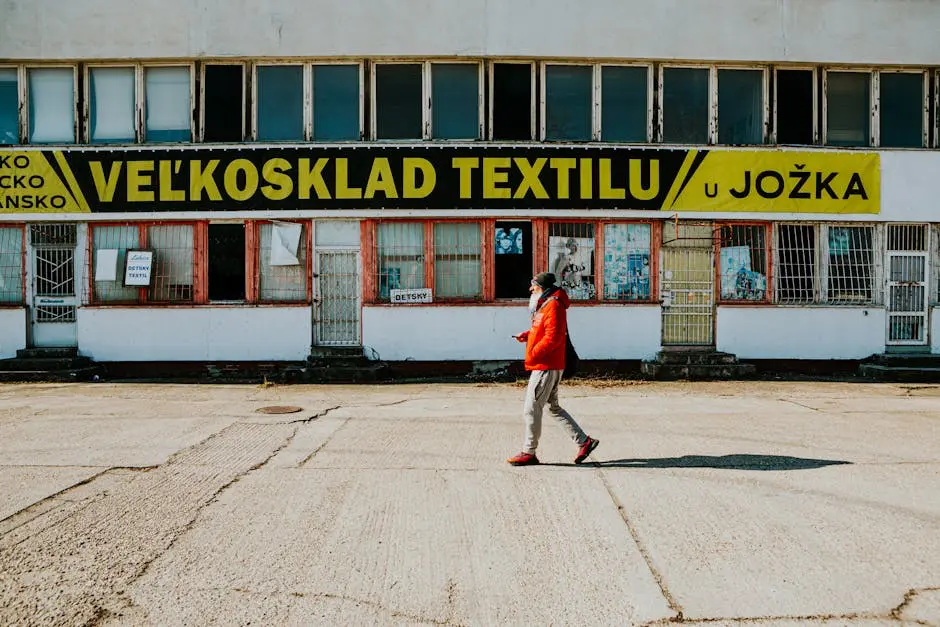 A man walks past a textile warehouse in Slovakia on a bright day, showcasing urban life.