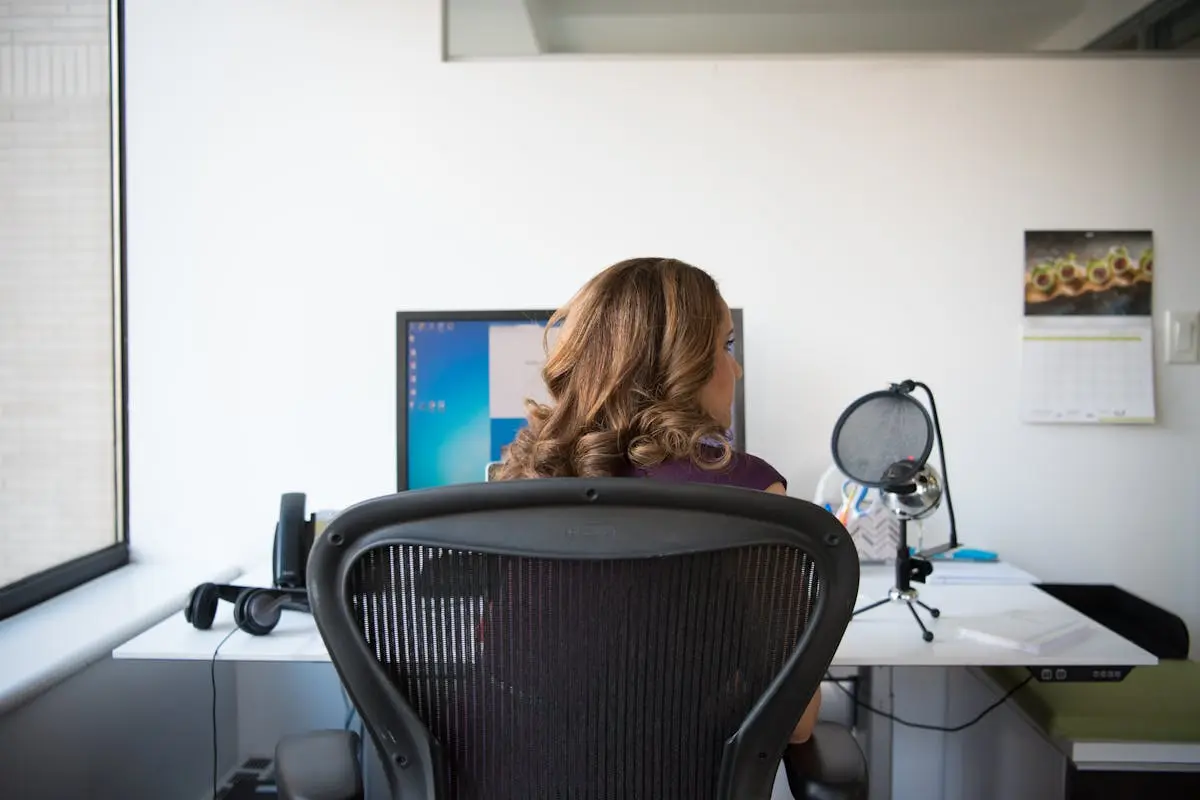 Adult woman working in a contemporary office setting with computer and microphone.