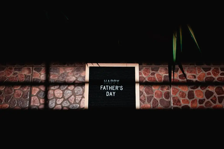 A wooden framed sign with ‘Happy Father’s Day’ on a stone-textured background, surrounded by shadows.