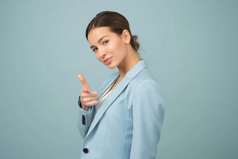 A young woman in a blue suit exhibits confidence with a relaxed pose against a blue background.