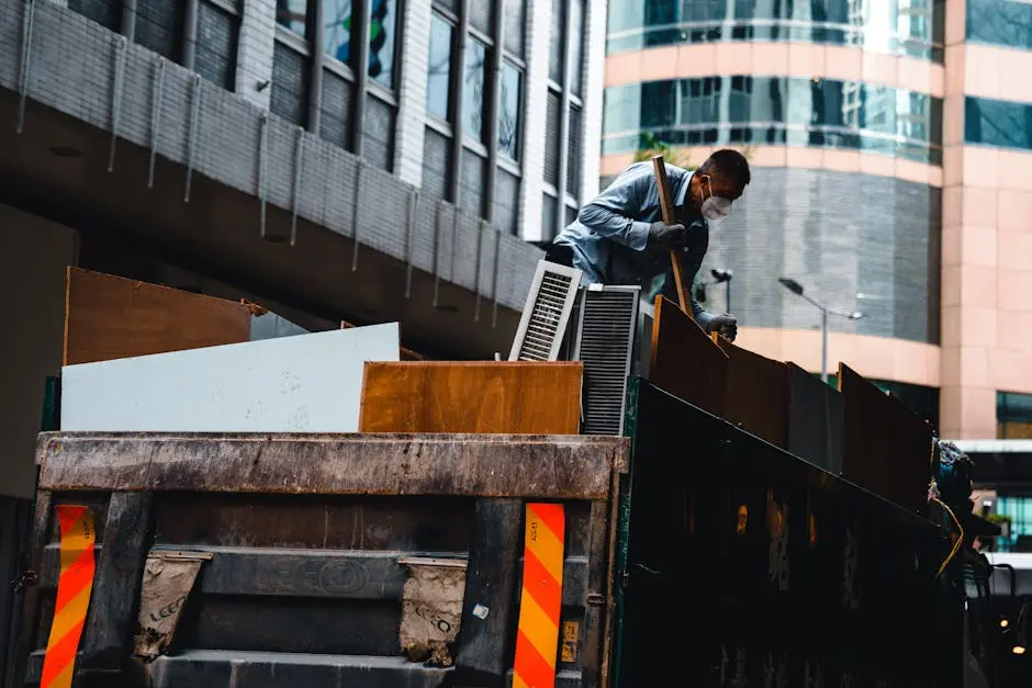 A man wearing a mask manages construction debris in a city environment from a large truck.